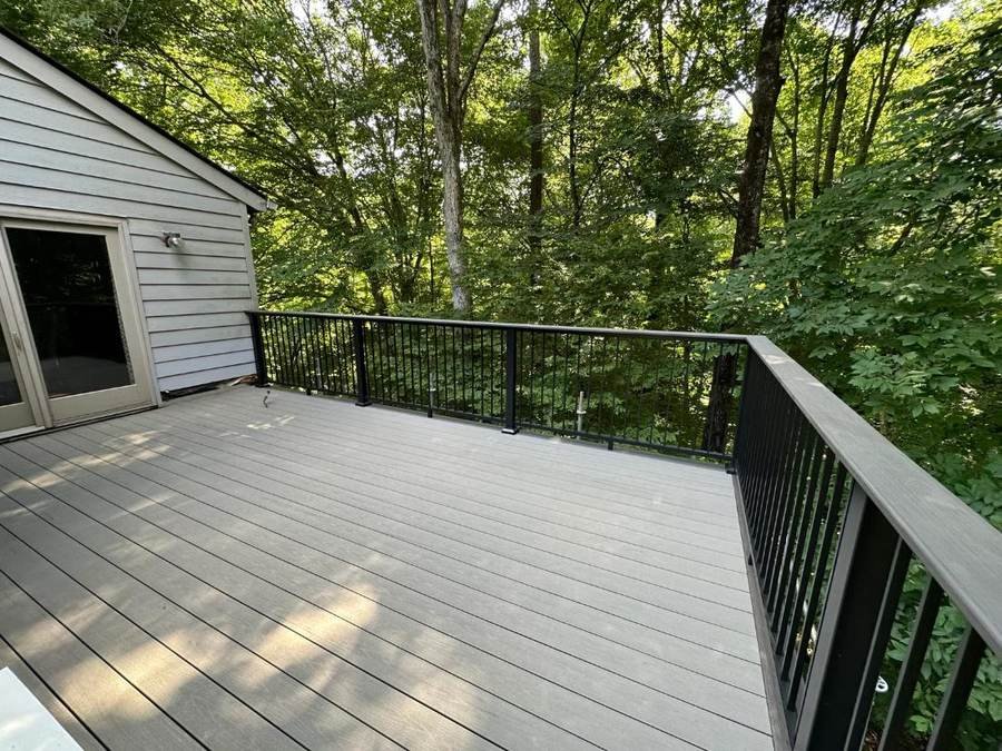 Grey composite deck boards with black aluminum railing overlooking woods